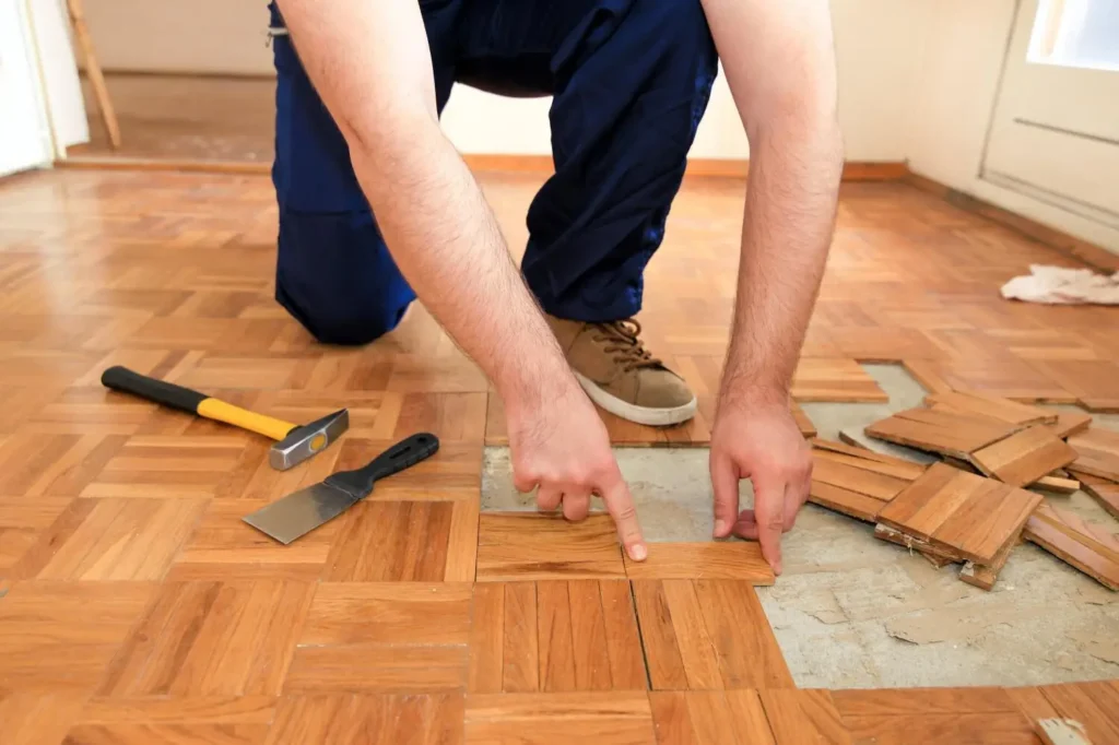 Hardwood floor repair in progress in Albany, NY, with a worker replacing damaged parquet tiles.